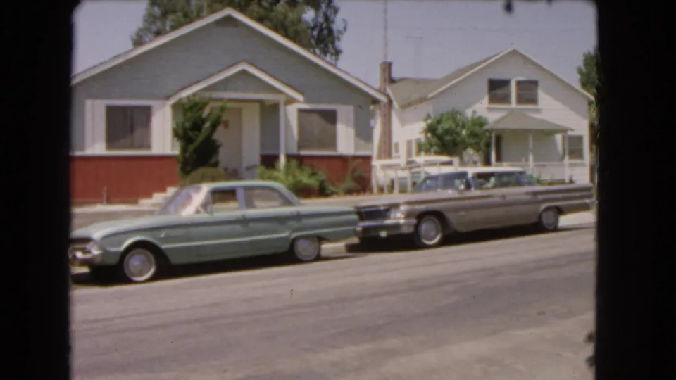 1966 Barstow frame with two parked mid-century cars, single-story houses, curb, trees, and visible 8mm film borders.