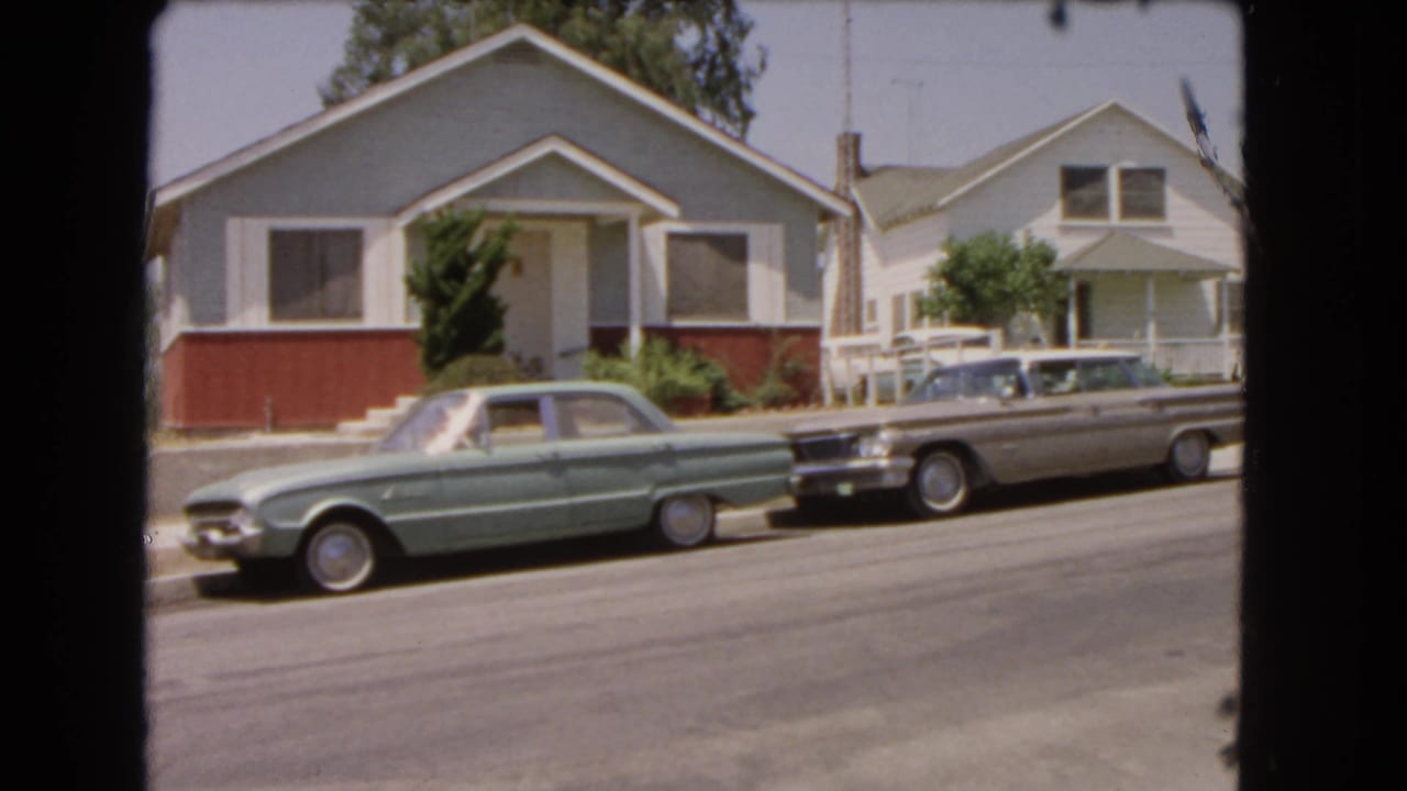 Static 8mm view of parked cars outside single-story homes in Barstow, California, in 1966.