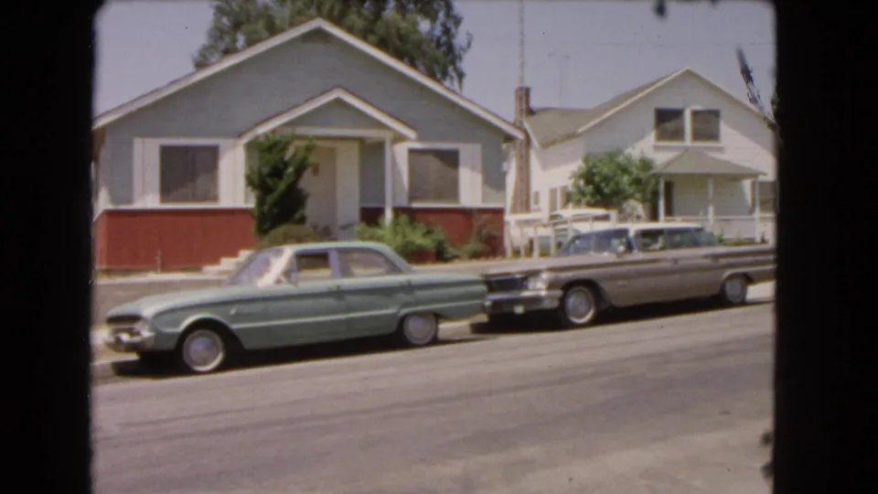1966 Barstow street scene showing two parked cars, a blue house, and a white house with porch.
