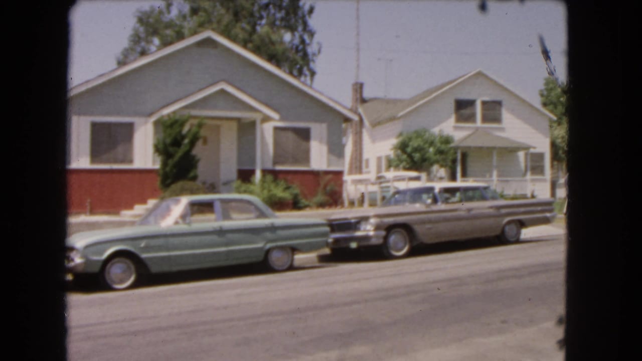 1966 Barstow residential street with a light green car and a silver sedan parked before modest single-story homes.
