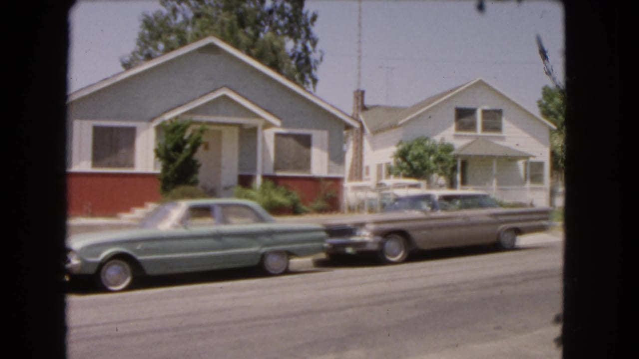 Parked cars and small homes seen from across a sunny residential street.
