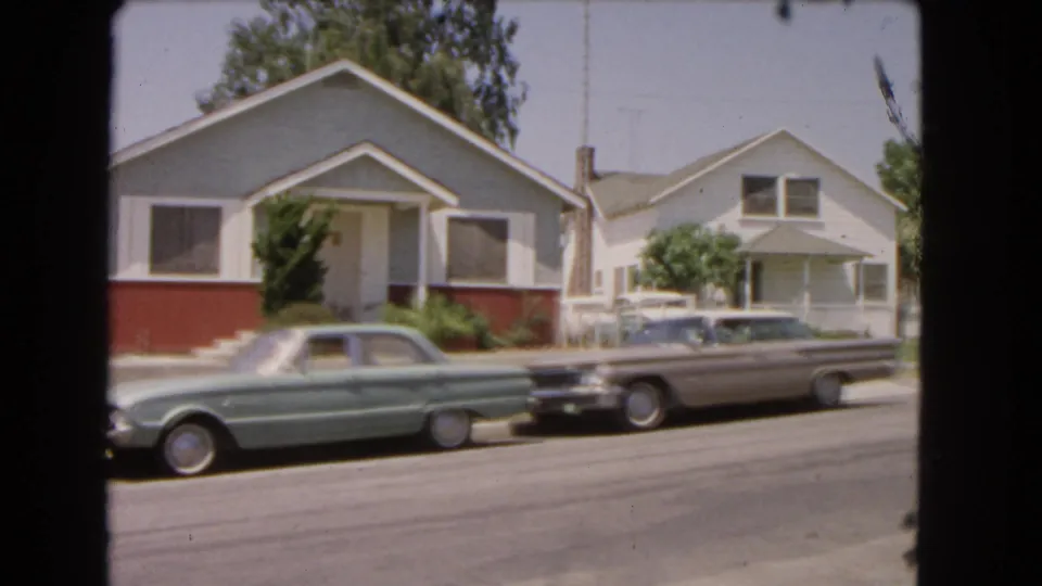 Barstow, California street view with parked mid-century cars, modest homes, and trees in a soft 8mm frame.