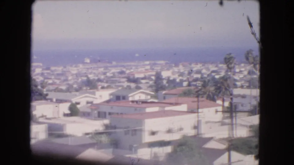 Soft 8mm overlook of Barstow rooftops, scattered trees, utility poles, and distant city blocks under haze.
