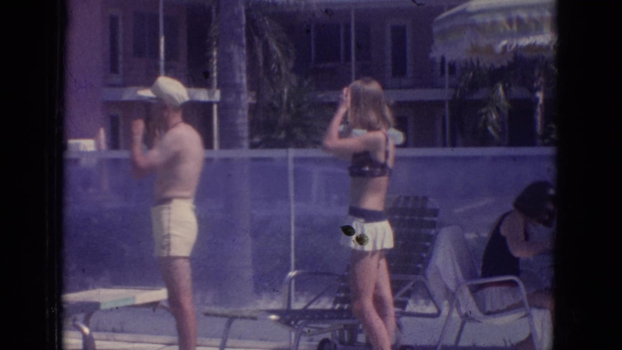 1966 Florida home-movie frame showing adults by a resort pool, including a man in a cap and a woman adjusting her hair.