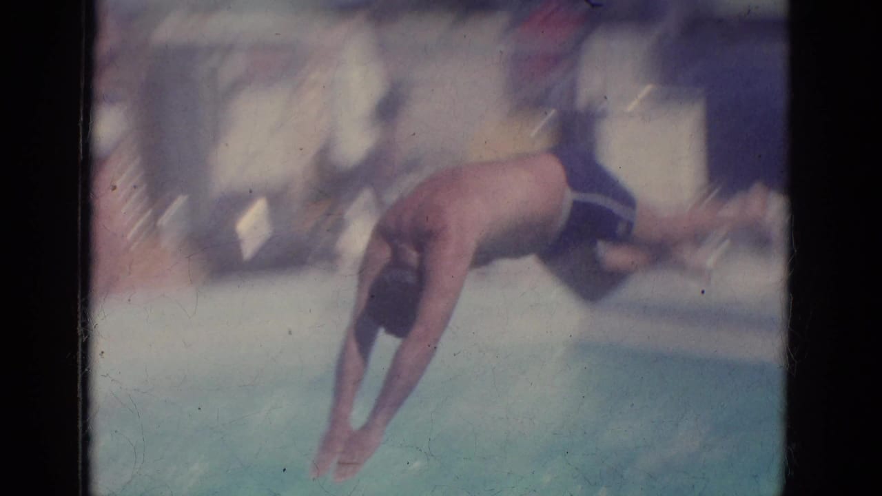 Adult man diving into a swimming pool, seen in soft 8mm color.