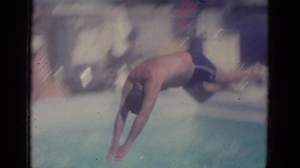 Adult man mid-dive into an outdoor pool in 1966 Florida home-movie footage, with soft focus and visible film edges.