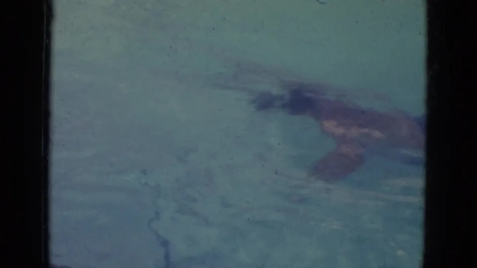 The swimmer appears underwater in the pool, partially obscured by water and the soft color of the 8mm scan.