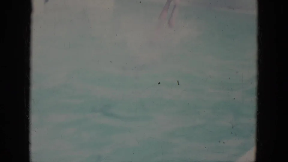 Faded 8mm frame shows blue-green pool water just after the dive, with part of the swimmer barely visible near the top of the frame.