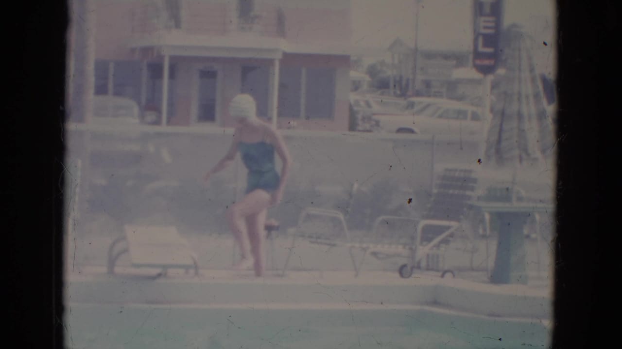 Woman steps onto or near a low diving board beside a motel pool.