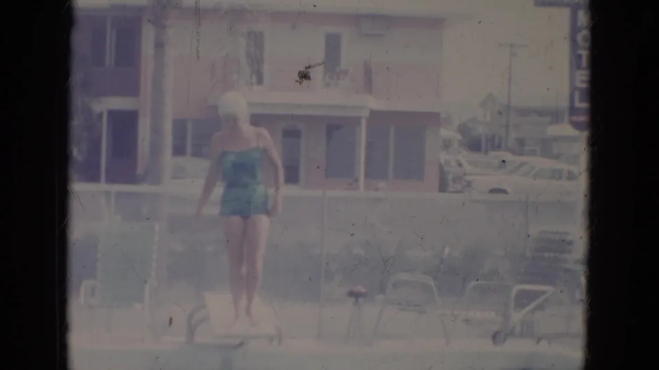 A faded 8mm frame shows the woman in a teal swimsuit near the diving board, with poolside chairs and a building in the background.