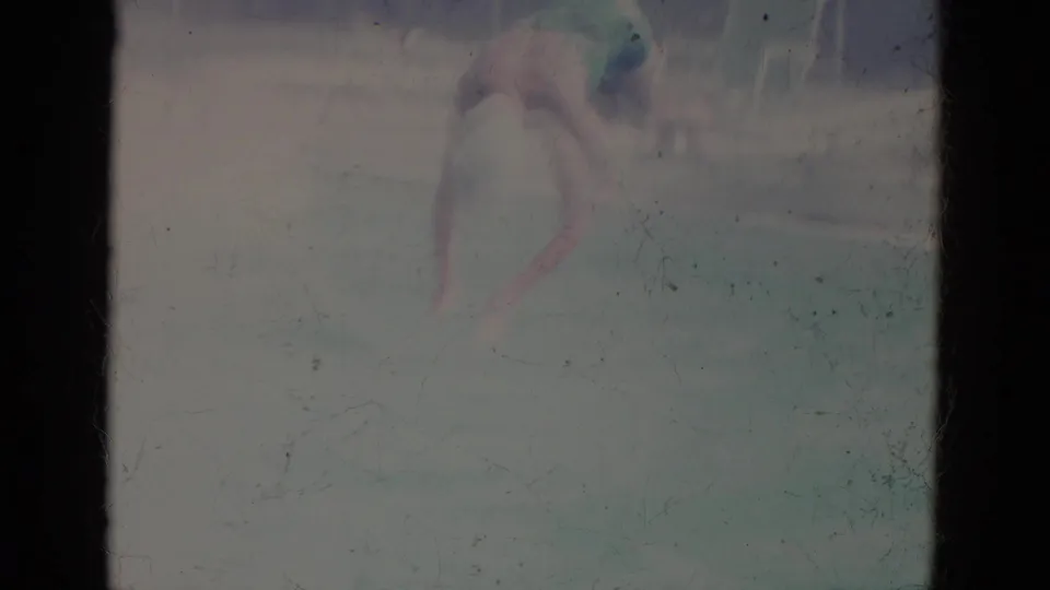 A hazy 8mm frame shows the swimmer in white cap partly obscured by bright pool water and film fading.