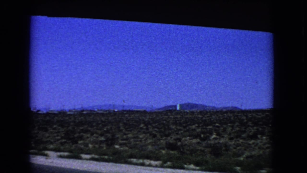 Open desert plain with low hills and a faint vertical structure on the horizon.