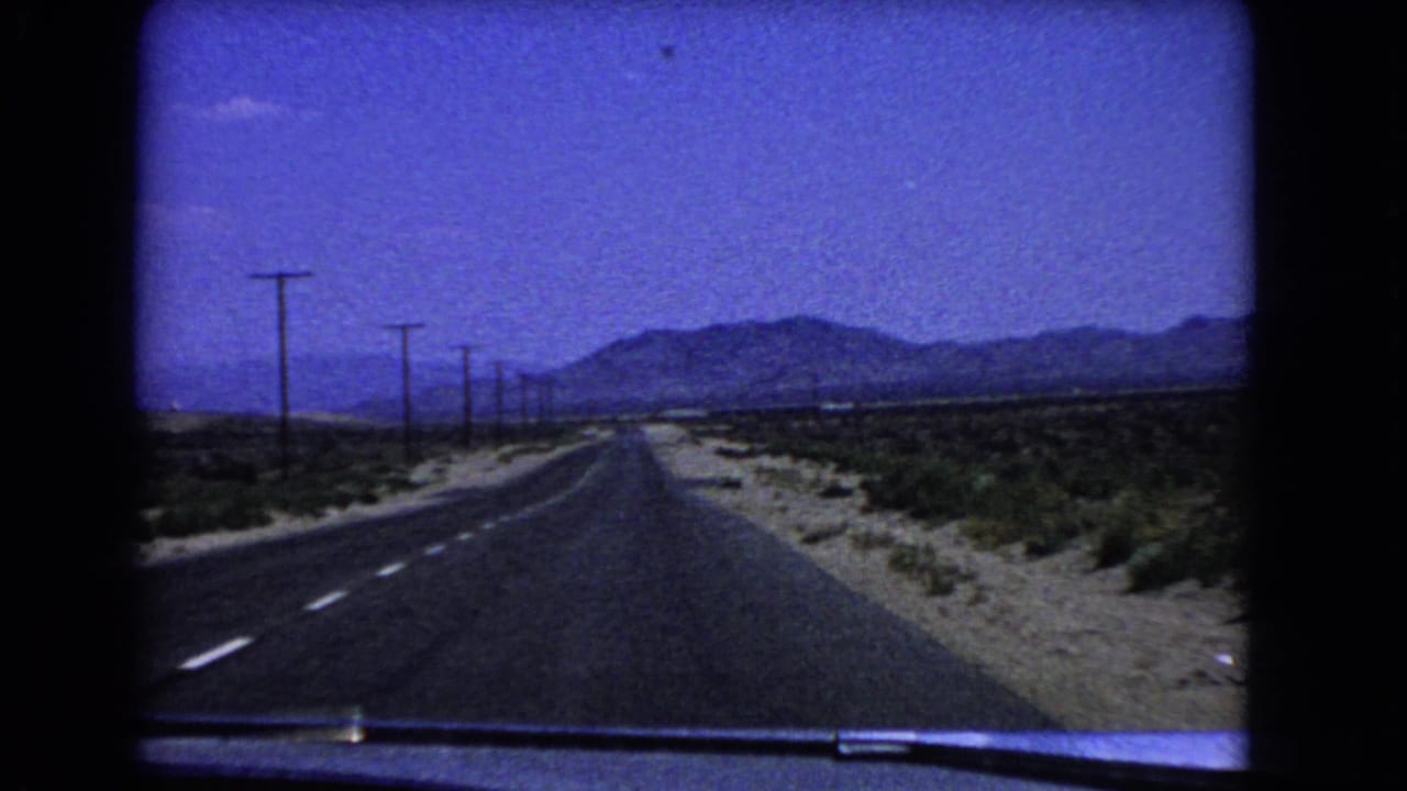 1966 California desert road viewed from inside a moving car, with utility poles along the highway and mountains ahead.