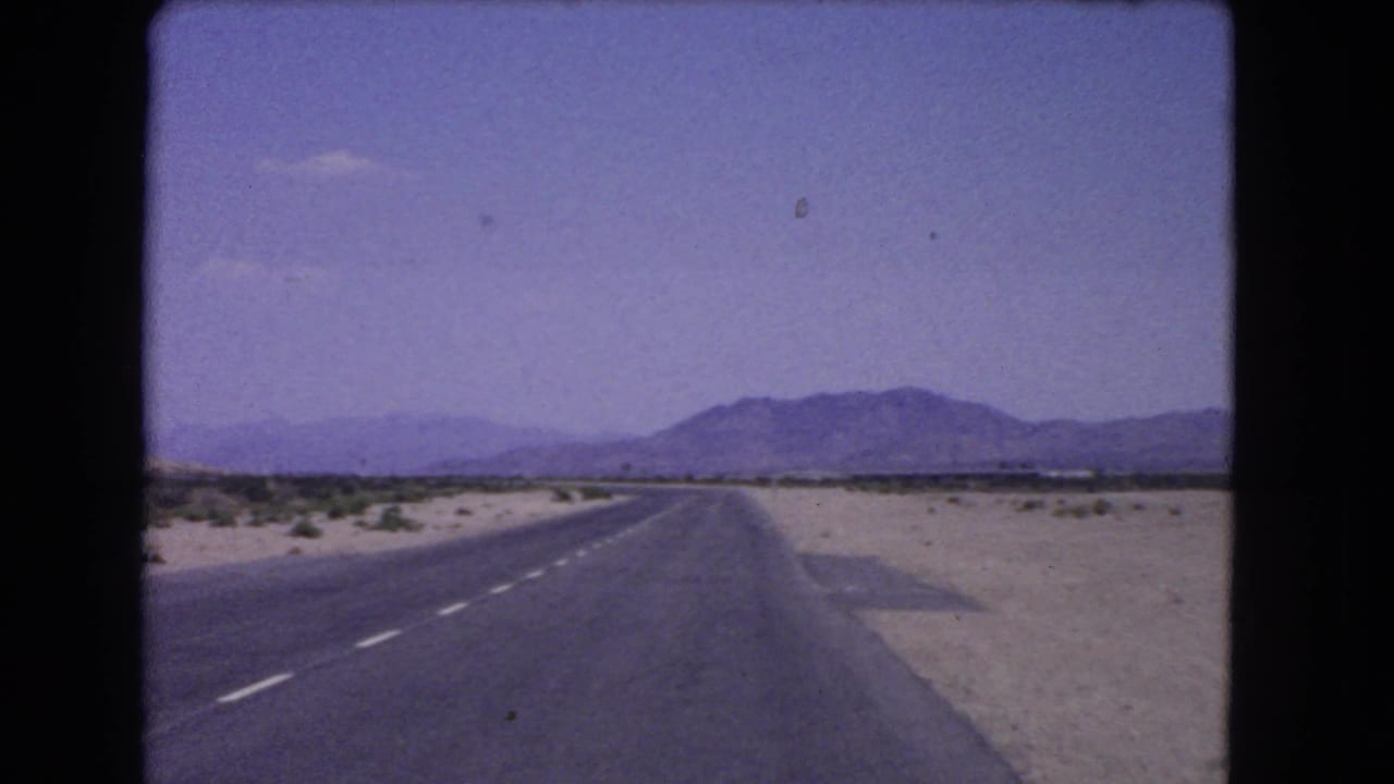 Open desert road curving slightly toward mountains under a pale sky.