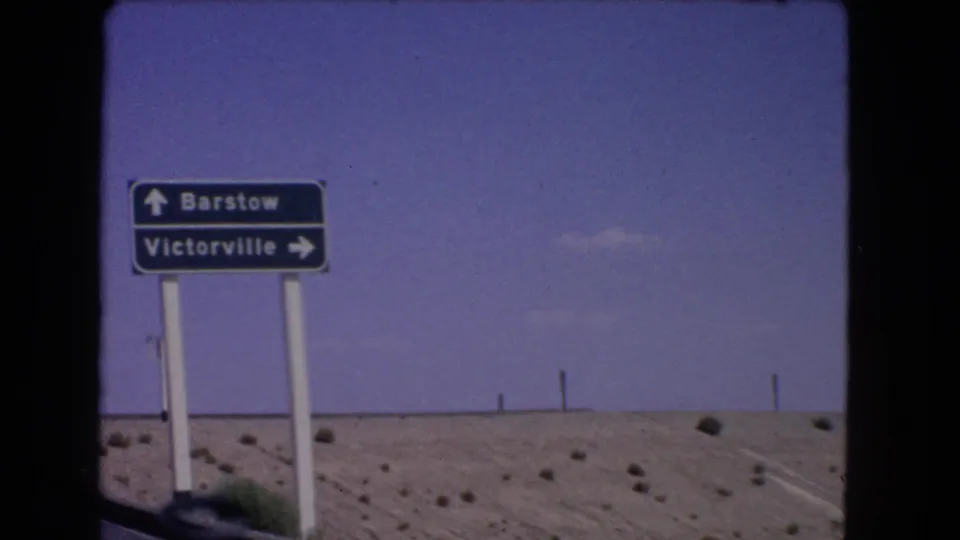 Clear 1966 8mm frame of a California road sign for Barstow and Victorville against desert scrub and open sky.