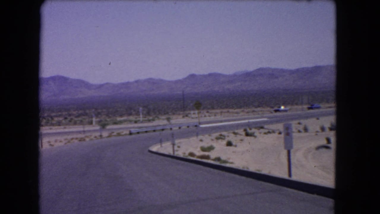 1966 California desert road scene with classic cars on a curving paved highway below distant mountains.