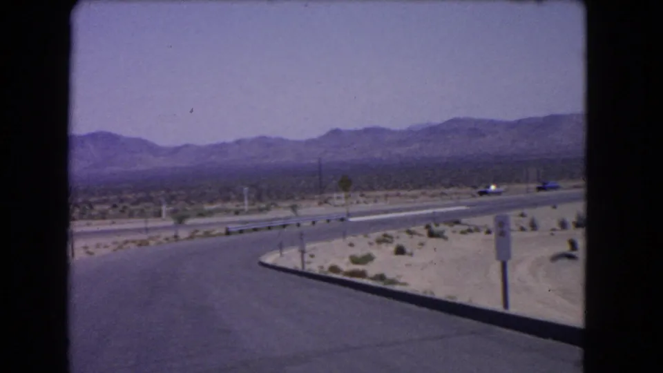 1966 California desert road scene with classic cars on a curving paved highway below distant mountains.