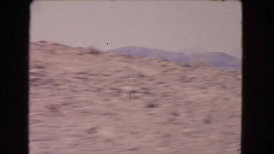1966 California home-movie frame with a soft, blurred view of desert hillside and distant mountains from a moving vehicle.