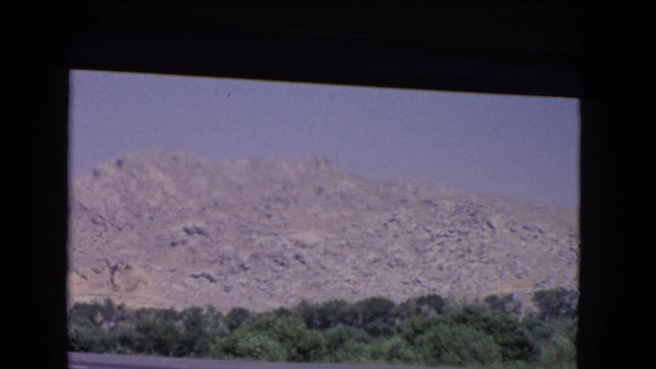 Rocky hillside and tree line viewed through a dark vehicle frame.