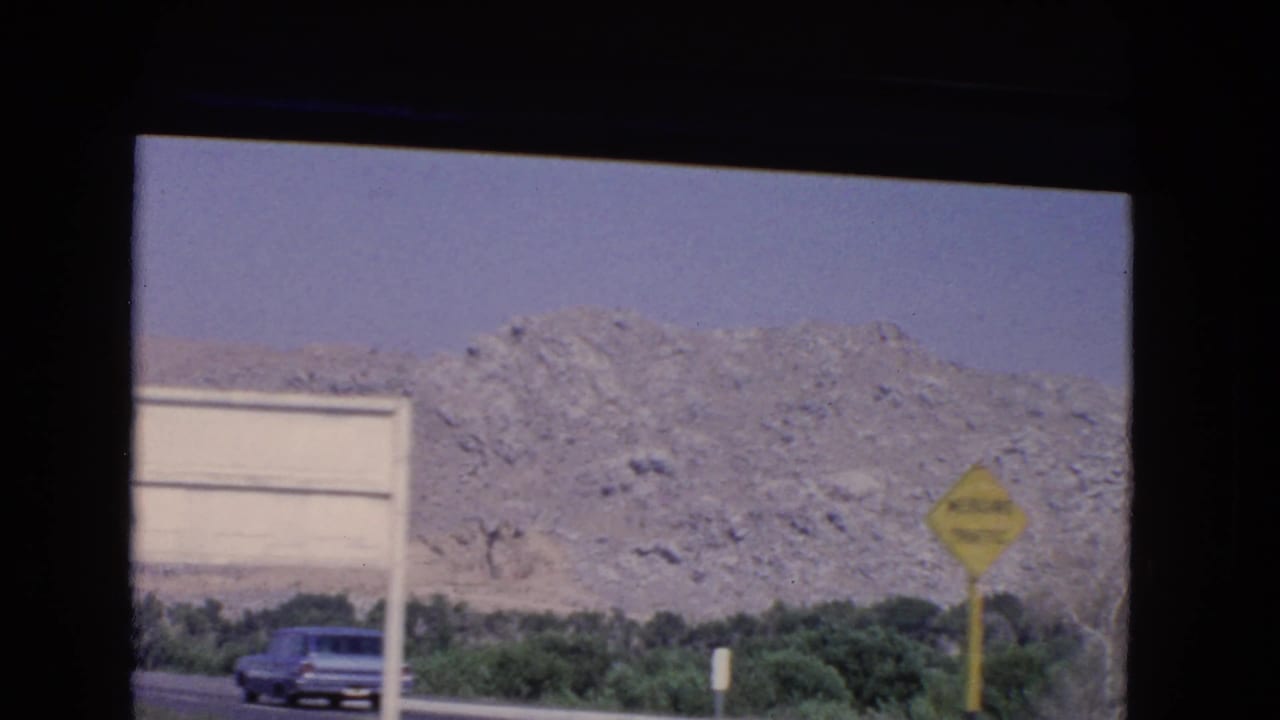 Rocky hillside beside a highway with an older car and a yellow roadside sign.