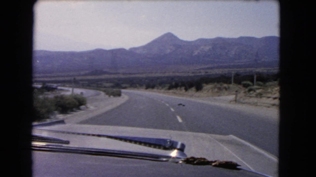 Winding highway ahead with car hood and windshield wiper in the foreground.