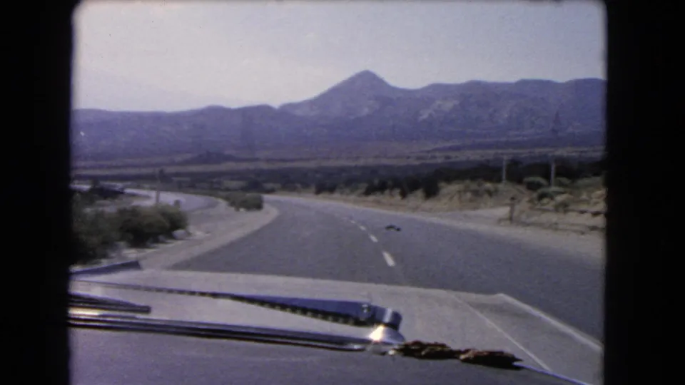 1966 California car-window view of a two-lane highway curving toward distant mountains across dry terrain.