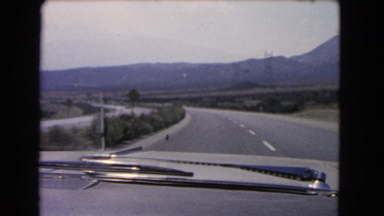 From inside the car, the road curves past a small sign in a hazy California mountain landscape from 1966.