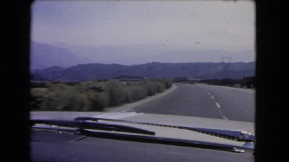 The final frame shows a windshield POV on a quiet California highway, with roadside brush, distant hills, and utility towers visible.