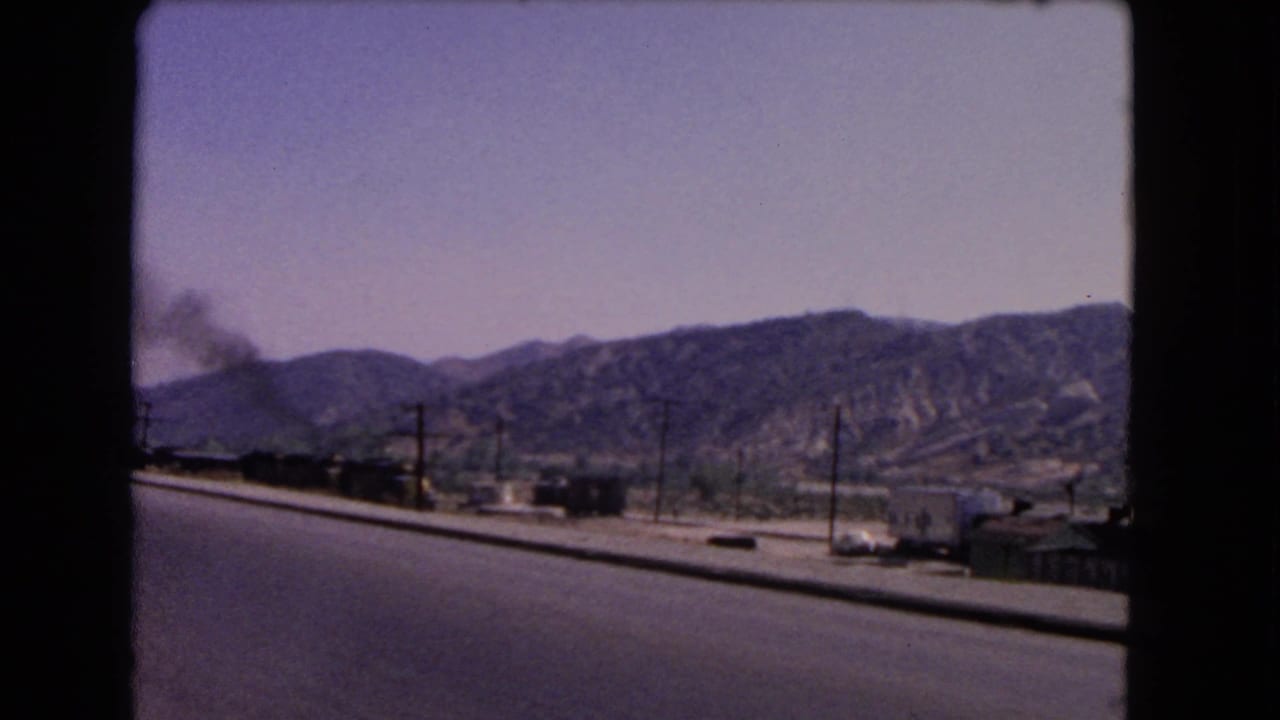 1966 California roadside scene with a smoke-producing train, utility poles, cars, and dry hills beyond the road.