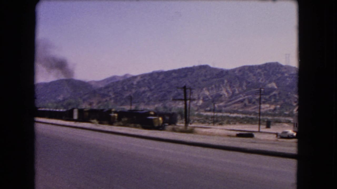 1966 California roadside view of a smoke-producing train running parallel to cars and utility poles below dry hills.