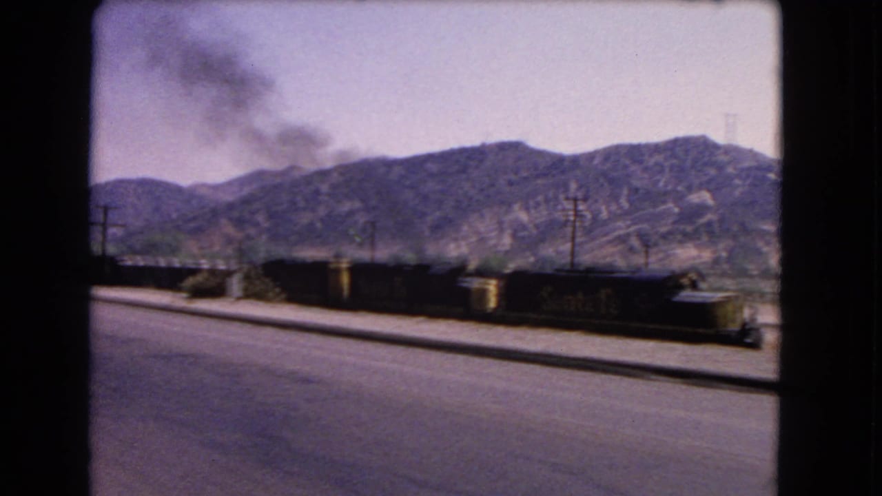 Freight cars and a smoke plume appear alongside a California mountain road in this 1966 8mm frame.