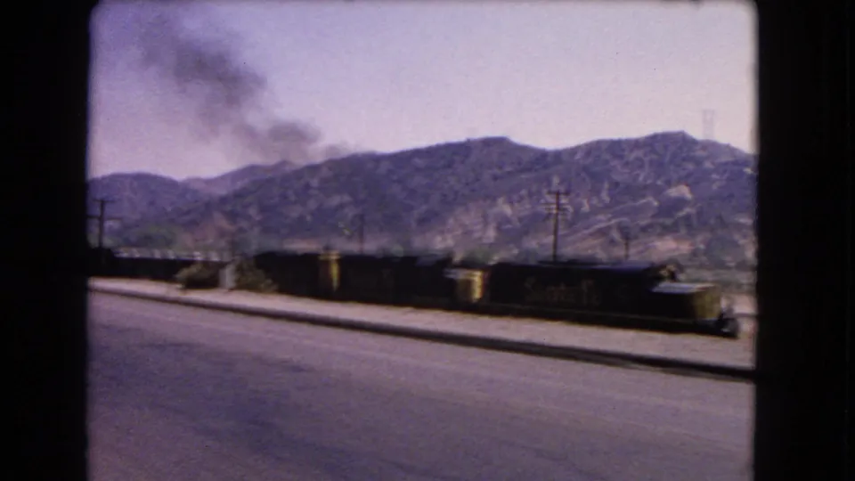 Freight cars and a smoke plume appear alongside a California mountain road in this 1966 8mm frame.