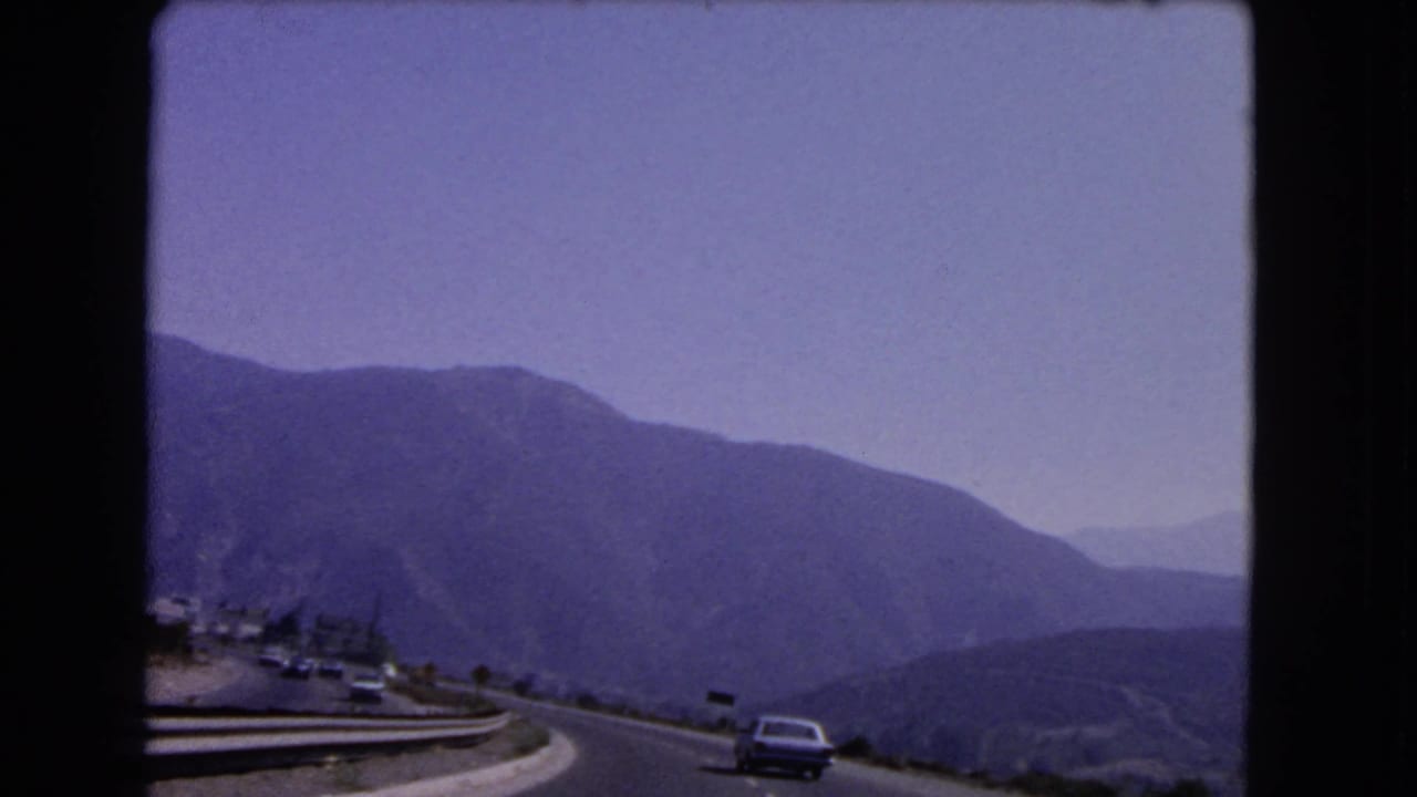 1966 California 8mm frame showing a mountain road with distant cars, guardrails, and hazy layered ridges.