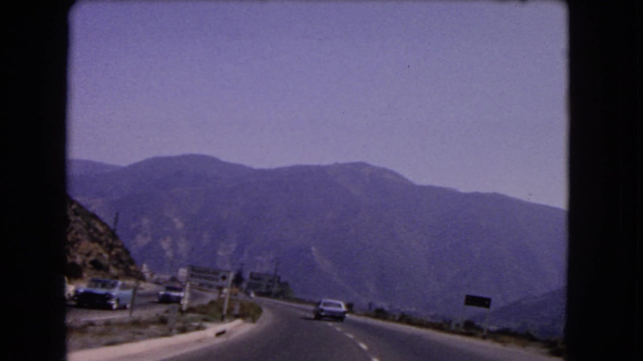 1966 California 8mm view from a moving car on a winding mountain highway with classic vehicles ahead.