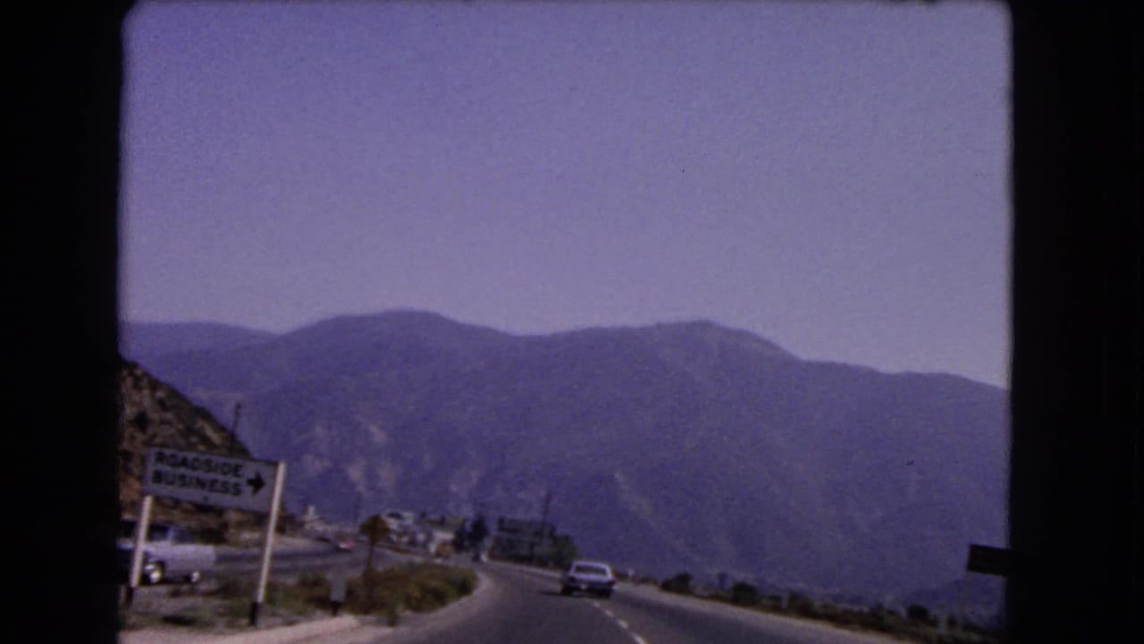 Roadside business sign beside a curving highway with mountains beyond.