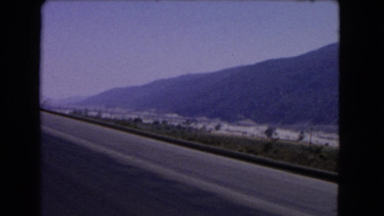 Open road beside a guardrail with a valley floor and dark mountain ridge in the distance.