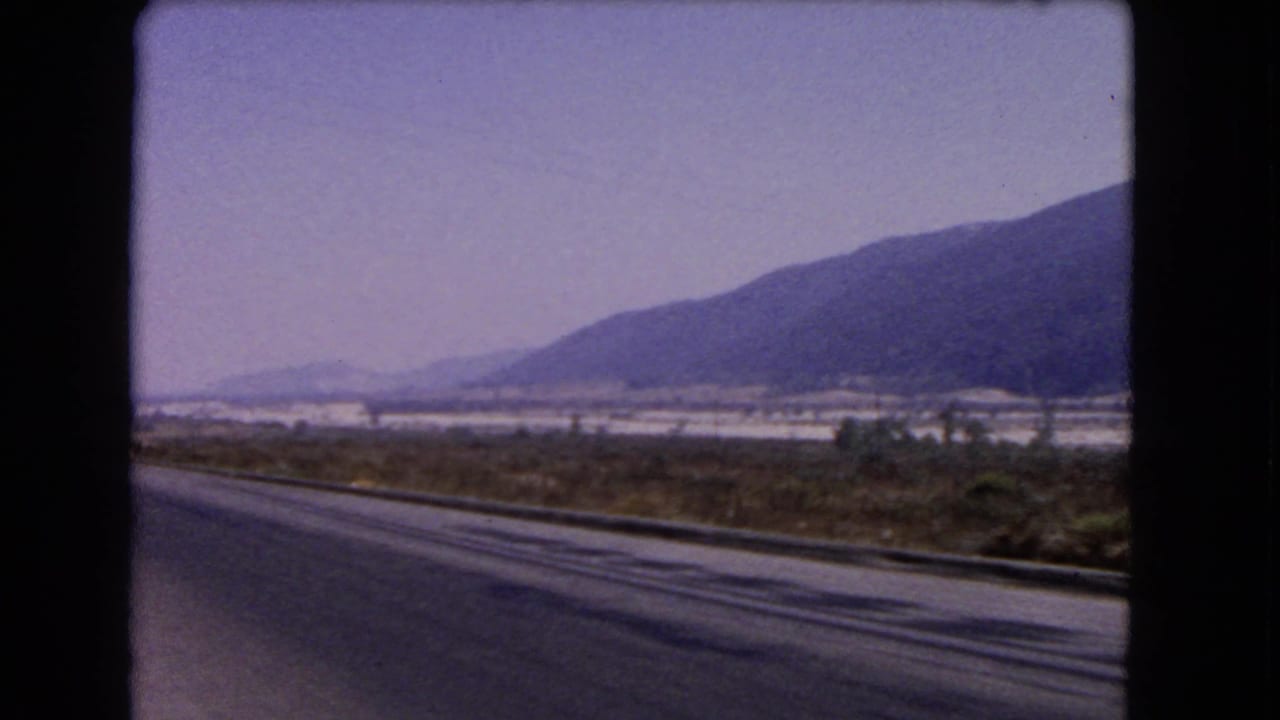 Roadside view of a mountain slope and open terrain from a moving car.