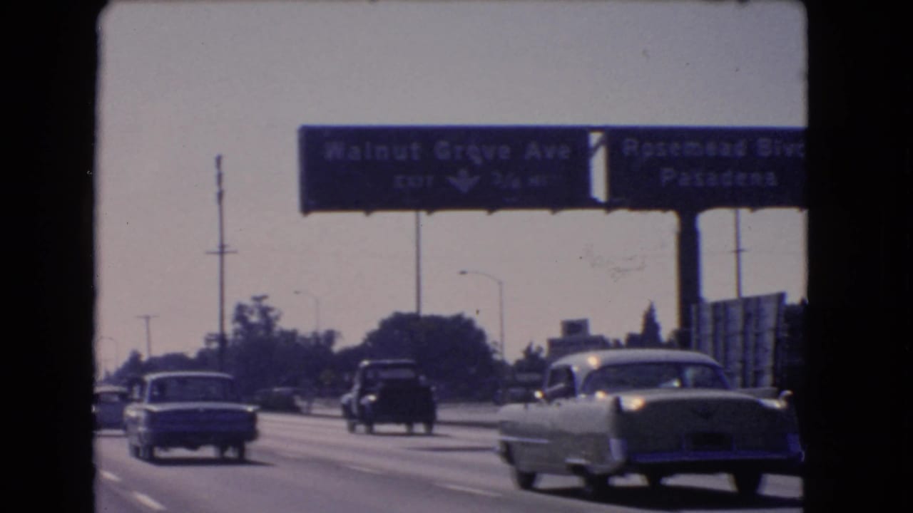 1966 California 8mm frame showing a light sedan, darker vehicles, and overhead signs above freeway lanes.