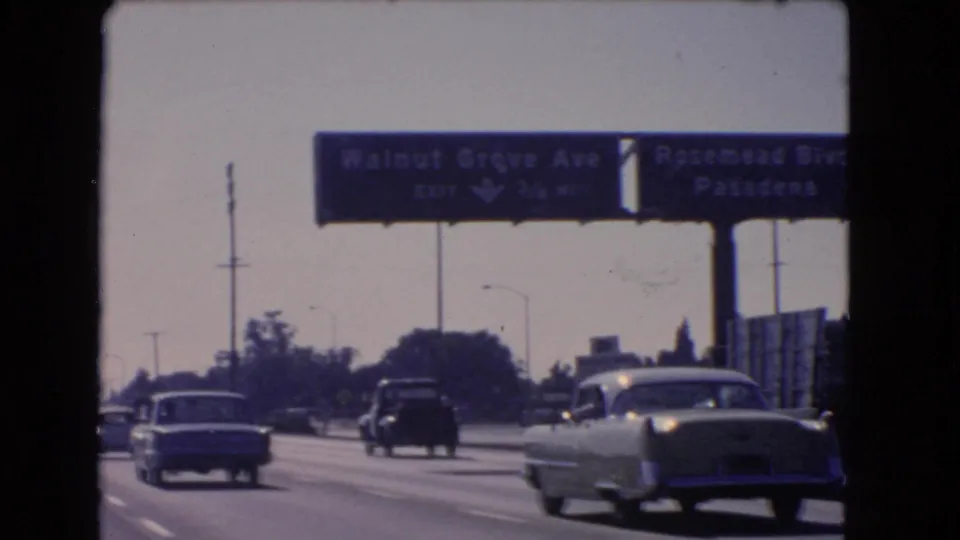 1966 California 8mm frame showing a light sedan, darker vehicles, and overhead signs above freeway lanes.