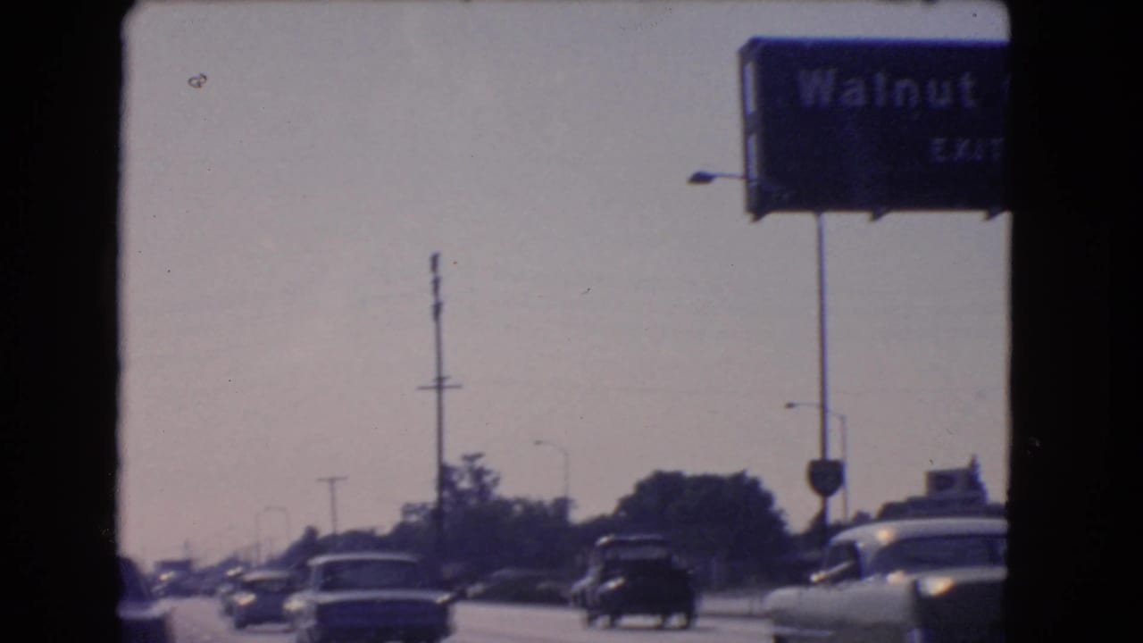 1966 California 8mm frame showing cars on a crowded highway beneath a blue Walnut Grove exit sign.