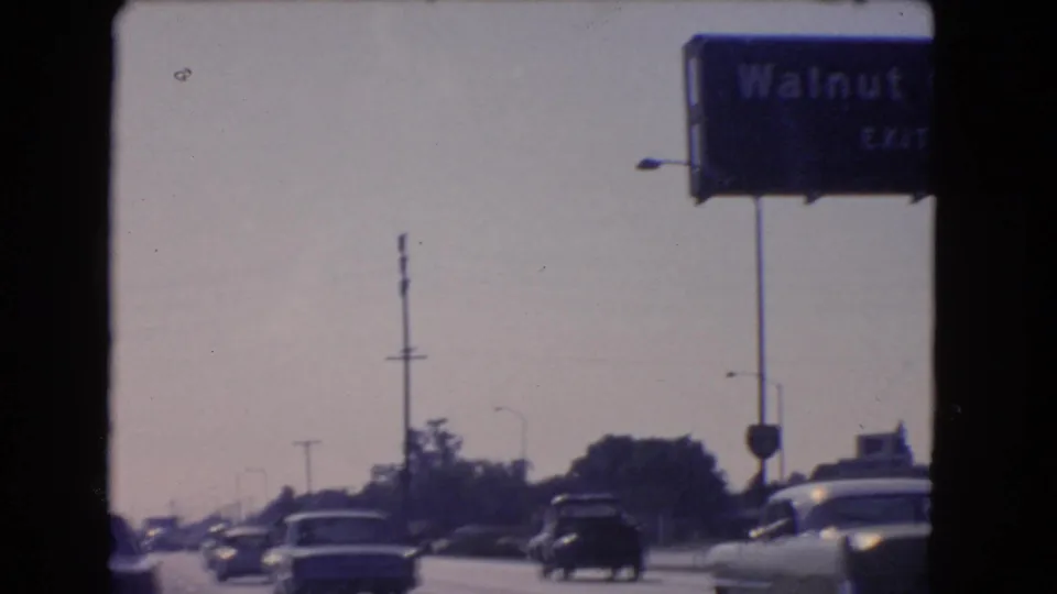 1966 California 8mm frame showing cars on a crowded highway beneath a blue Walnut Grove exit sign.