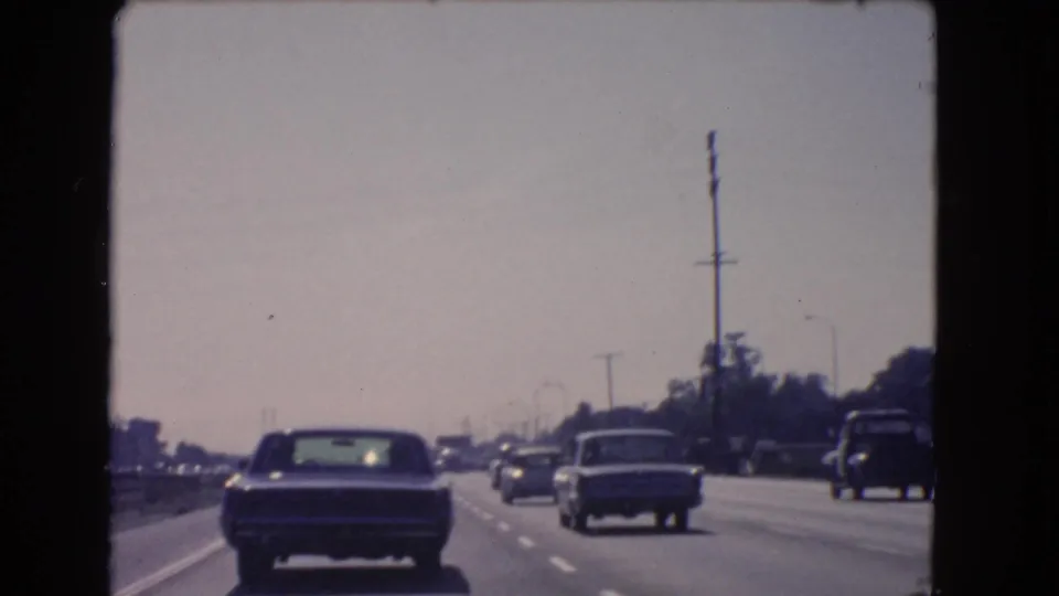 1966 California highway view with sedans and a pickup truck traveling in steady daytime traffic.