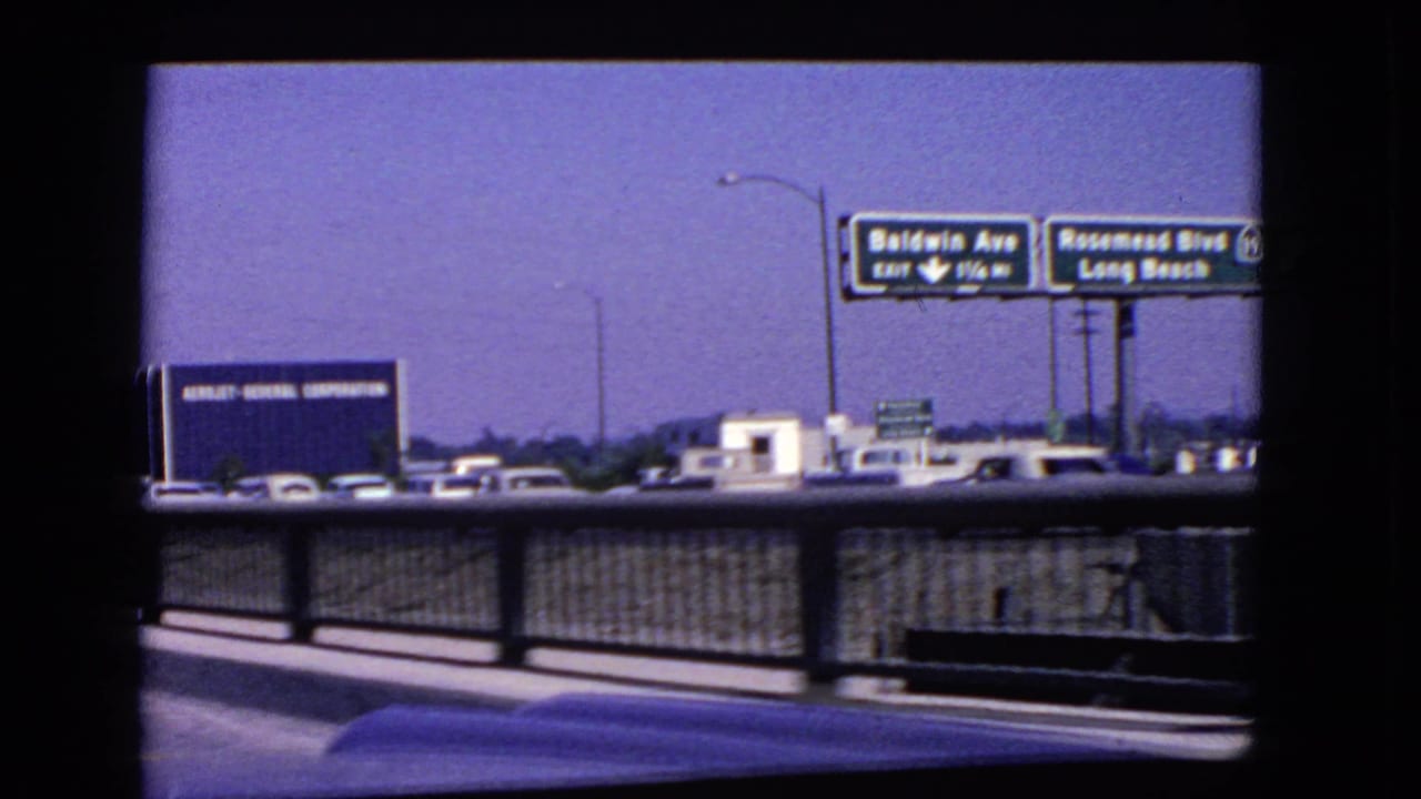 1966 California highway view with Baldwin Ave and Rosemead Blvd signs, traffic, guardrail, lamp posts, and a blue industrial sign in the distance.