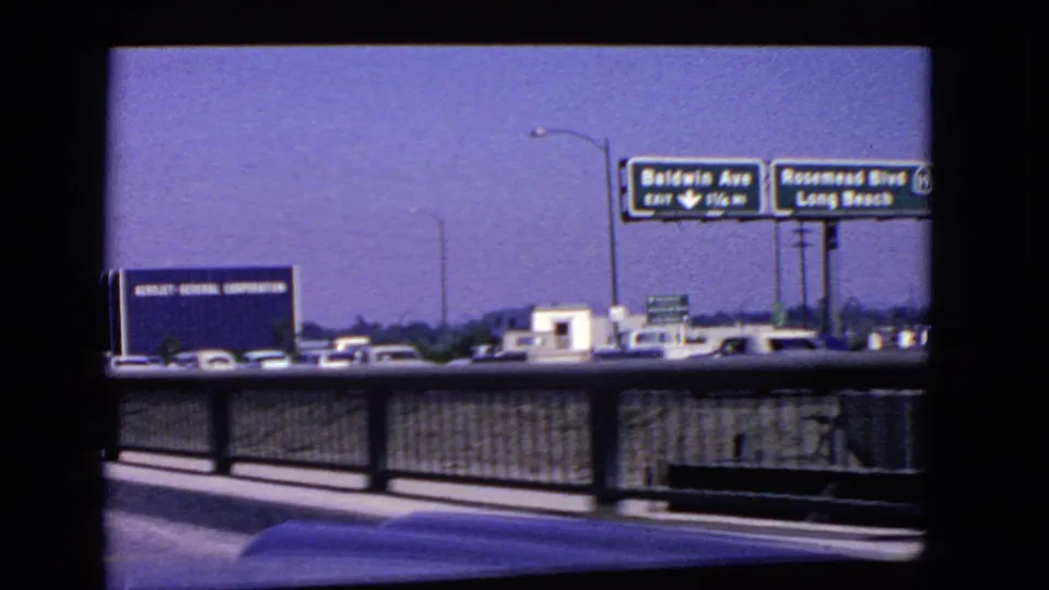 1966 California highway view with Baldwin Ave and Rosemead Blvd signs, traffic, guardrail, lamp posts, and a blue industrial sign in the distance.