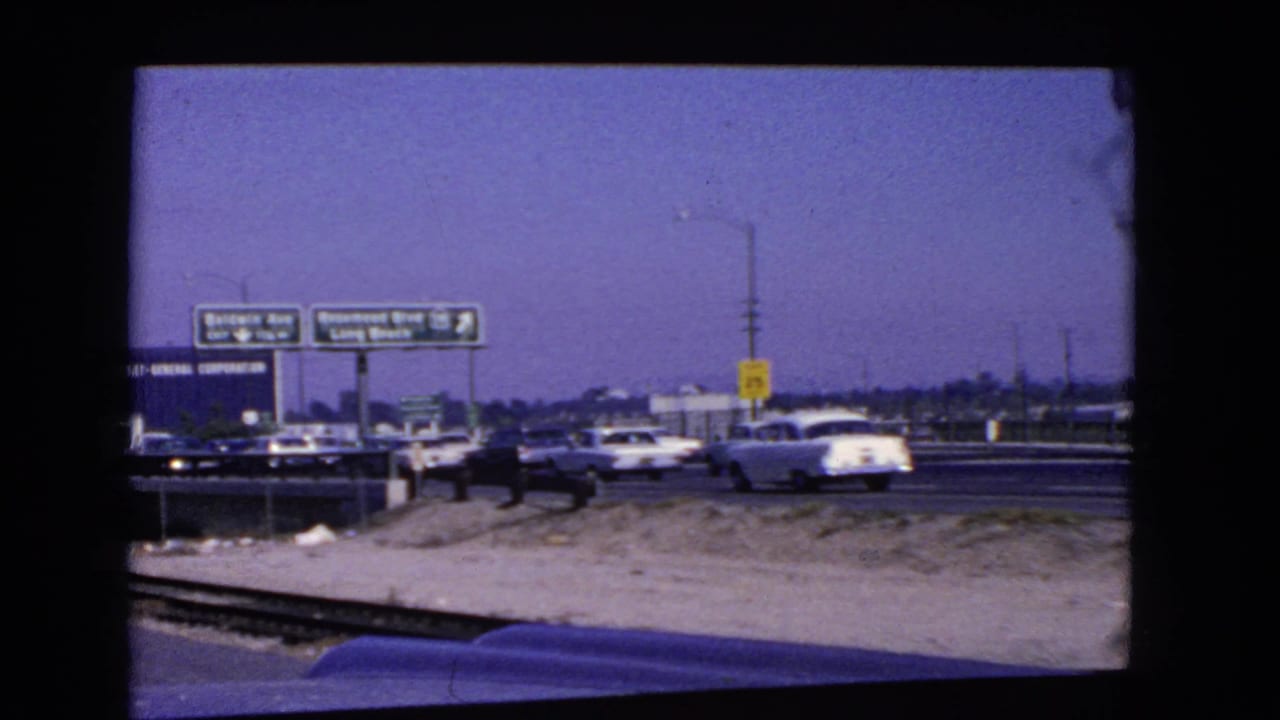 Cars in freeway traffic pass under overhead guide signs with a yellow speed sign nearby.