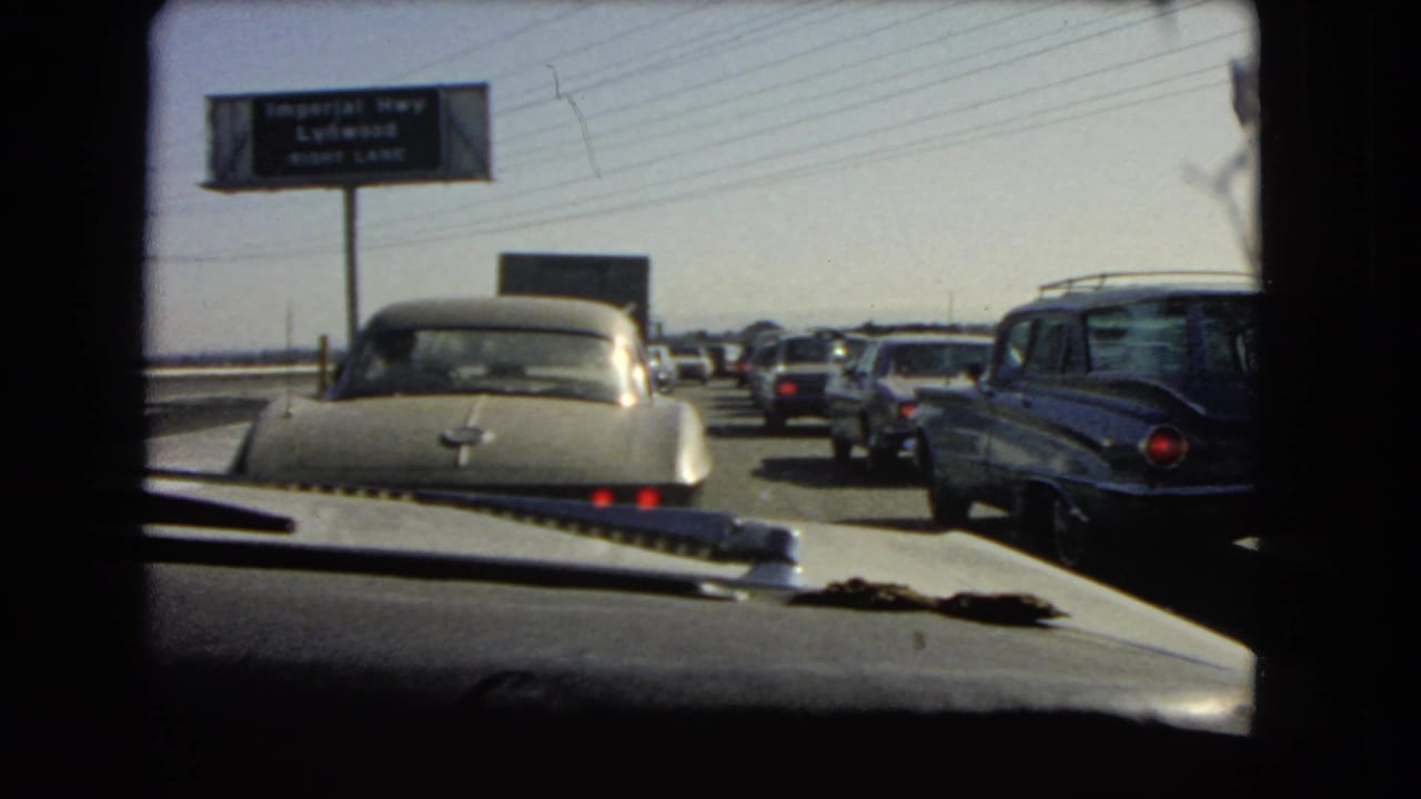1966 California 8mm view from inside a car in slow traffic, with mid-century vehicles and an overhead Imperial Hwy area sign.