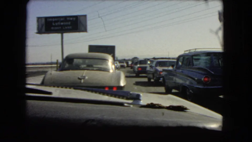 1966 California 8mm view from inside a car in slow traffic, with mid-century vehicles and an overhead Imperial Hwy area sign.