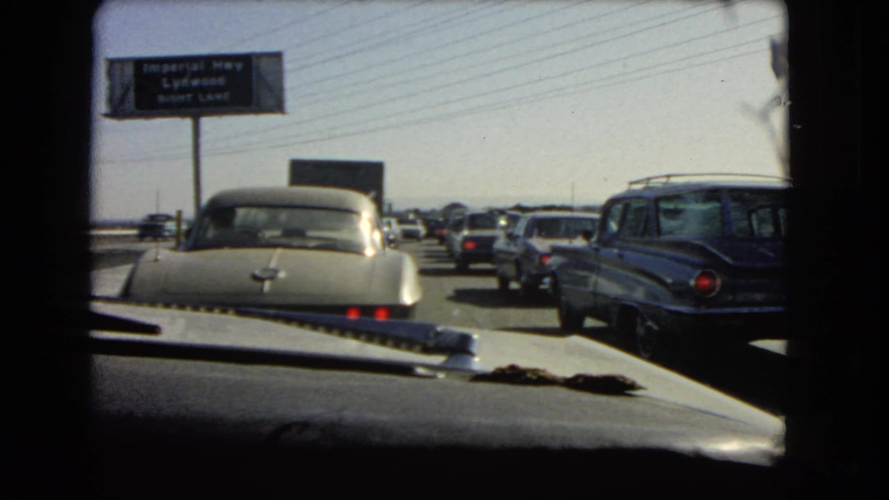 Slow highway traffic with a station wagon at right and a road sign in the distance.