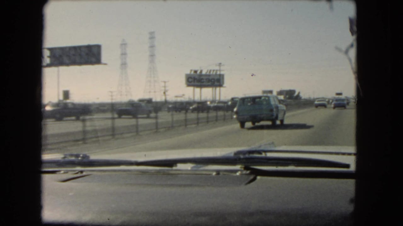 1966 California in-car highway shot with vehicles moving ahead, power towers, roadside signs, and a billboard reading Chicago.