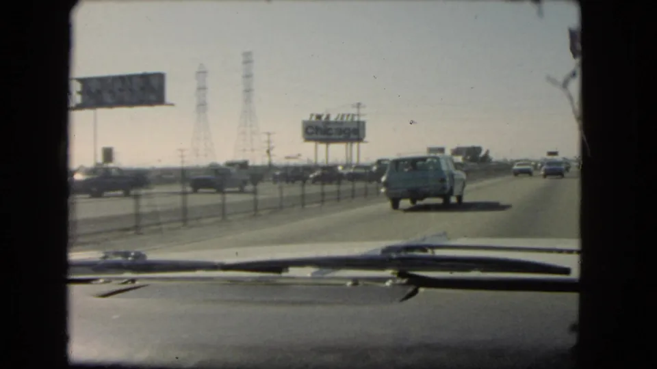1966 California in-car highway shot with vehicles moving ahead, power towers, roadside signs, and a billboard reading Chicago.